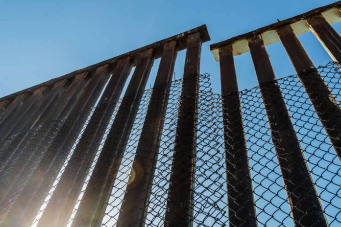 View of a border wall with a chain-link fence against a clear blue sky
