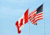 Canadian and American flags waving against a blue sky