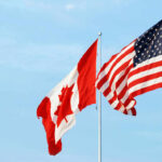 Canadian and American flags waving against a blue sky