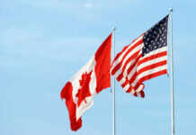 Canadian and American flags waving against a blue sky