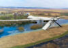 A military drone flying over a rural landscape with a river