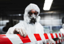 Worker in protective gear holding a red and white barrier tape in an industrial environment