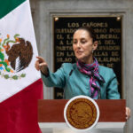 A government official delivering a speech in front of the Mexican flag