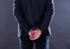 A man in a suit with hands cuffed behind his back
