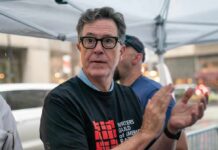 A man in a black t-shirt with a writers' guild logo clapping at a public event