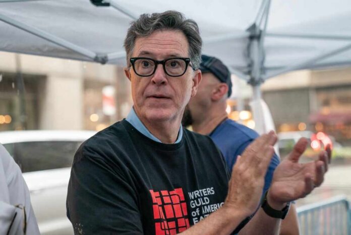 A man in a black t-shirt with a writers' guild logo clapping at a public event