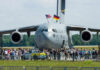A large military aircraft with flags, surrounded by a crowd at an airshow