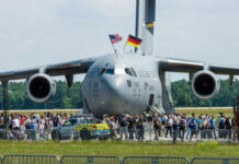 A large military aircraft with flags, surrounded by a crowd at an airshow
