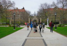 Students walking along a pathway on a university campus with historic buildings in the background