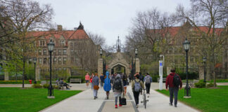 Students walking along a pathway on a university campus with historic buildings in the background