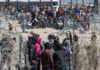 A crowd of people at a border area with law enforcement and barbed wire