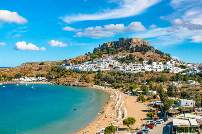 A picturesque coastal view featuring a beach, a historic castle on a hill, and a Mediterranean village
