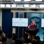 A woman speaking at a podium during a White House press briefing with journalists in attendance