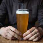Beer Panic Hits Boston Person holding a glass of craft beer in a bar
