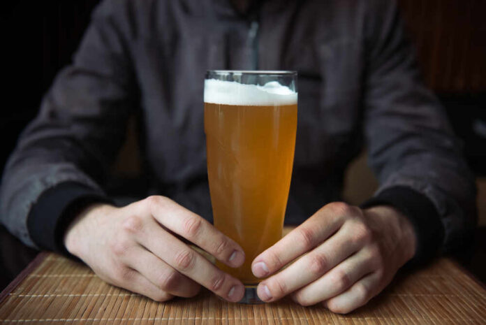 Man,Holding,Glass,Of,Beer Person holding a glass of craft beer in a bar