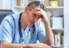 doctor in scrubs sitting with hand on forehead
