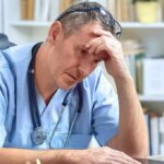 doctor in scrubs sitting with hand on forehead