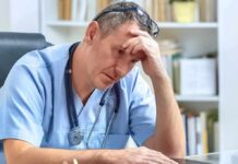 doctor in scrubs sitting with hand on forehead