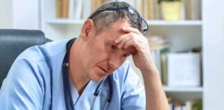 doctor in scrubs sitting with hand on forehead
