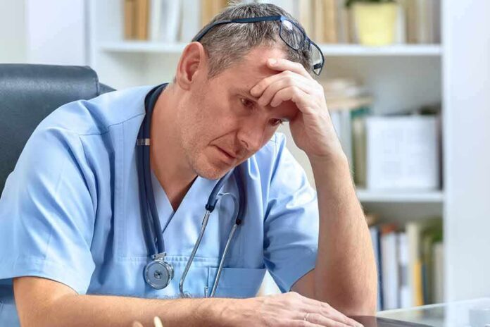 doctor in scrubs sitting with hand on forehead