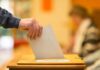 Hand placing a ballot into a wooden voting box