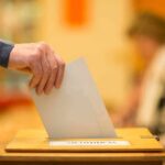 Hand placing a ballot into a wooden voting box
