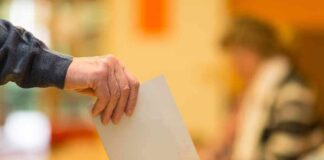 Hand placing a ballot into a wooden voting box