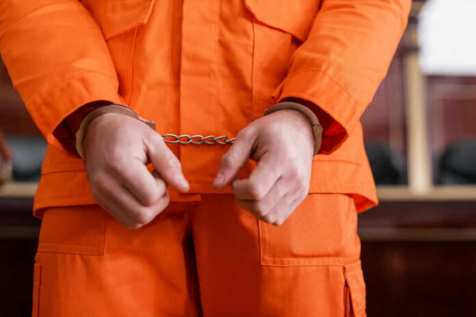 shutterstock_2121704996 A person in an orange jumpsuit with handcuffs