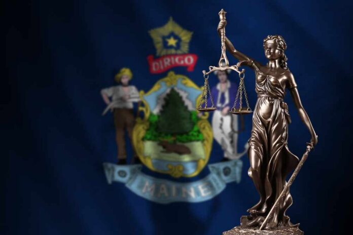 Bronze statue of Lady Justice in front of the Maine state flag