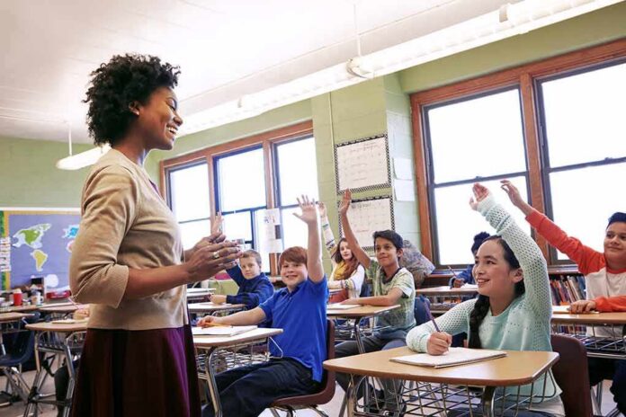 shutterstock_2250724177-1 Teacher engaging with students raising hands in a classroom