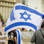 ICC Warrant Hangs Over Netanyahu Person holding an Israeli flag at a public demonstration