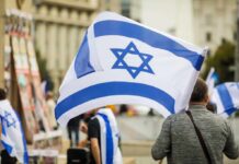 ICC Warrant Hangs Over Netanyahu Person holding an Israeli flag at a public demonstration
