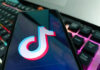 Close-up of a smartphone displaying the TikTok logo on its screen, with a colorful keyboard in the background