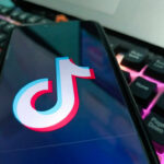 Close-up of a smartphone displaying the TikTok logo on its screen, with a colorful keyboard in the background