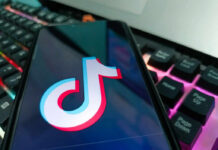 Close-up of a smartphone displaying the TikTok logo on its screen, with a colorful keyboard in the background