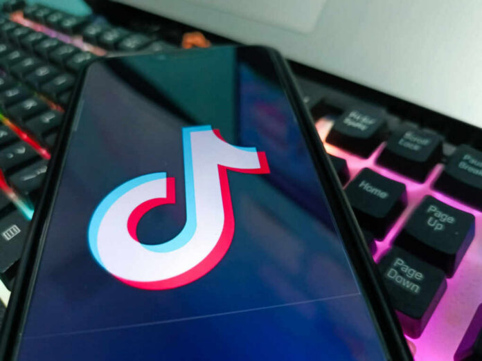 Close-up of a smartphone displaying the TikTok logo on its screen, with a colorful keyboard in the background