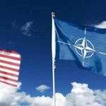 NATO flag and a blurred United States flag against a blue sky