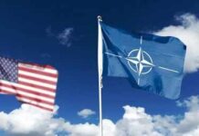 NATO flag and a blurred United States flag against a blue sky