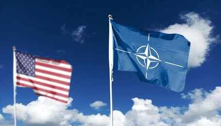 NATO flag and a blurred United States flag against a blue sky