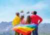 Group of friends with rainbow flags facing mountains
