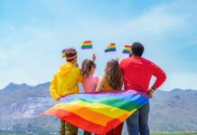 Group of friends with rainbow flags facing mountains