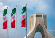 Three Iranian flags in front of the Azadi Tower against a blue sky