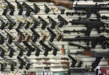 ATF Unmasks Massive Straw-Buy Ring Wall display with handguns and rifles for sale.