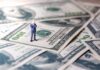 Miniature businessman standing on US dollar bills
