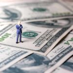 Miniature businessman standing on US dollar bills