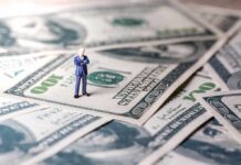 Miniature businessman standing on US dollar bills