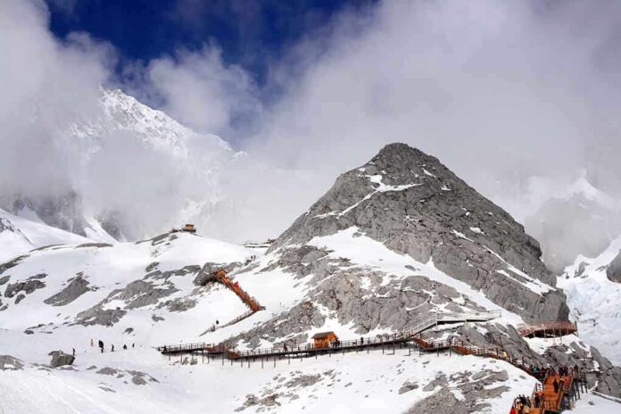 Snow-covered mountain with hiking trails and tourists under a cloudy sky