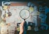 Hand holding magnifying glass over investigation board