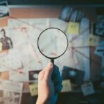 Hand holding magnifying glass over investigation board