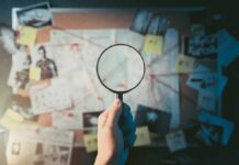 Hand holding magnifying glass over investigation board